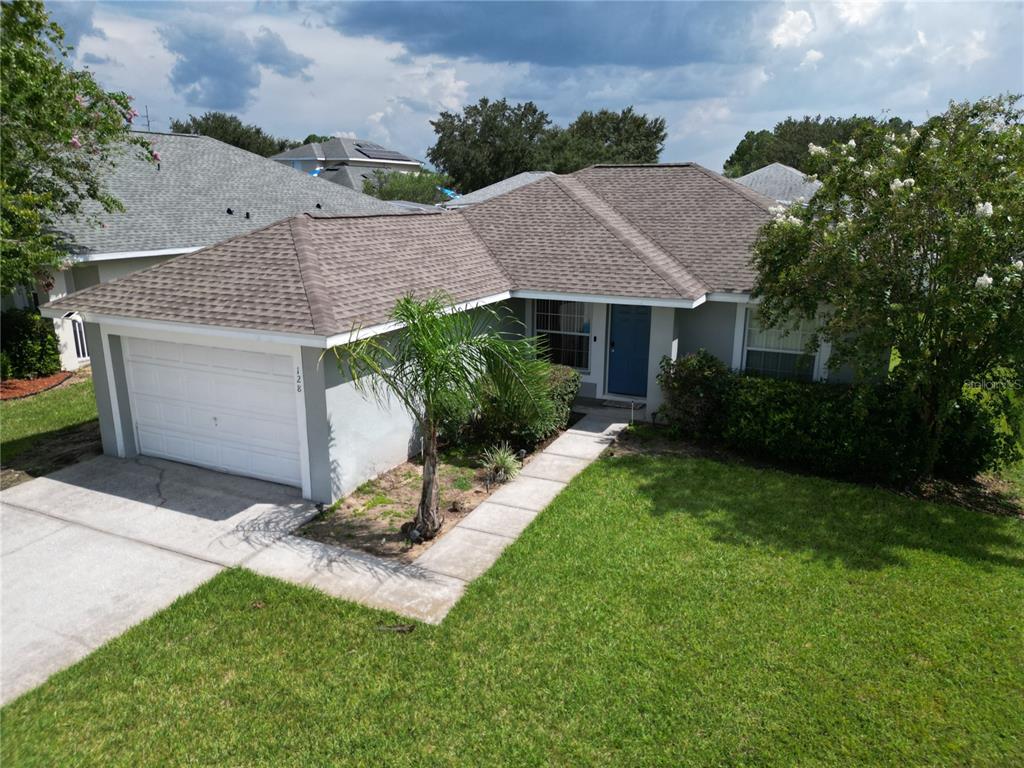 An aerial view shows a single-story house with a gray roof, white garage, and front lawn — 128 PINE CONE DRIVE, DAVENPORT, FL