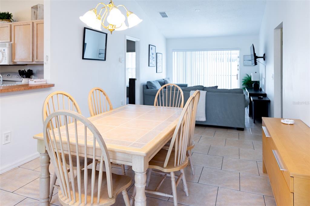 A dining area with a tiled table and wooden chairs sits adjacent to a living room — 128 PINE CONE DRIVE, DAVENPORT, FL