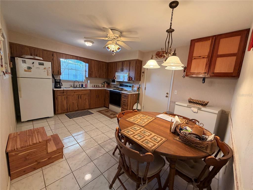 A kitchen with wood cabinets, white appliances, tile flooring, and a round dining table — 1640 JUNO TR UNIT 205B, ASTOR, FL