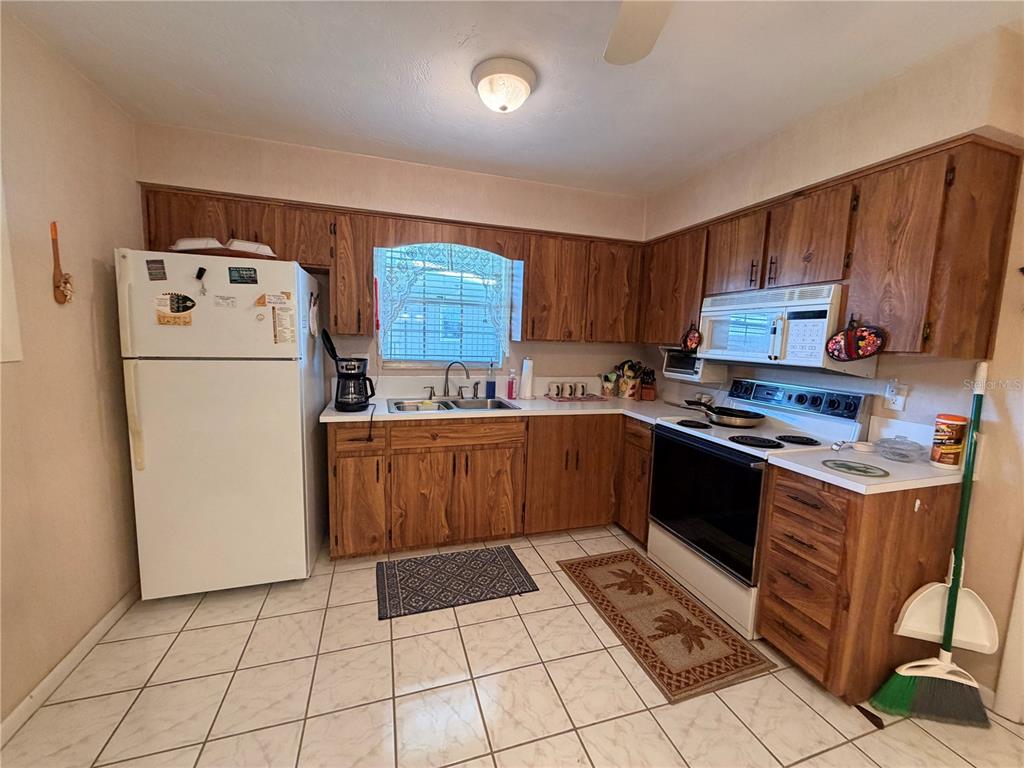 A kitchen features wood cabinets, white appliances, tiled floors, and a window above the sink — 1640 JUNO TR UNIT 205B, ASTOR, FL