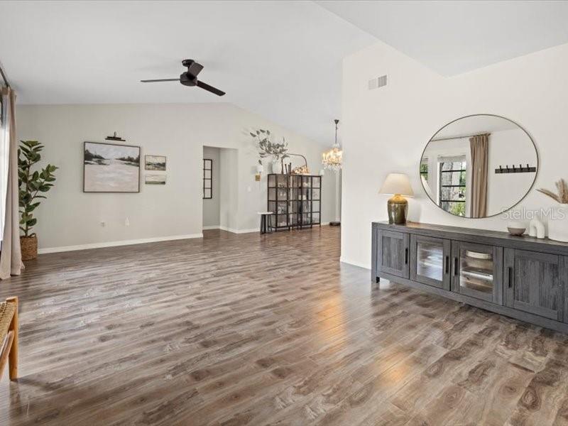 A spacious living room features wood-look flooring, a ceiling fan, and a large round wall mirror — 15650 PRARIE CREEK BLVD, PUNTA GORDA, FL