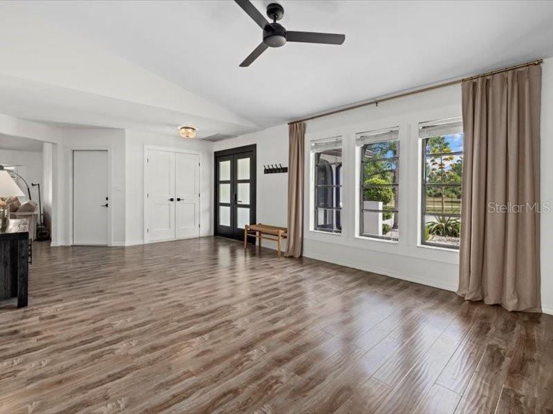 A spacious room features wood-look flooring, a ceiling fan, and large windows with curtains — 15650 PRARIE CREEK BLVD, PUNTA GORDA, FL