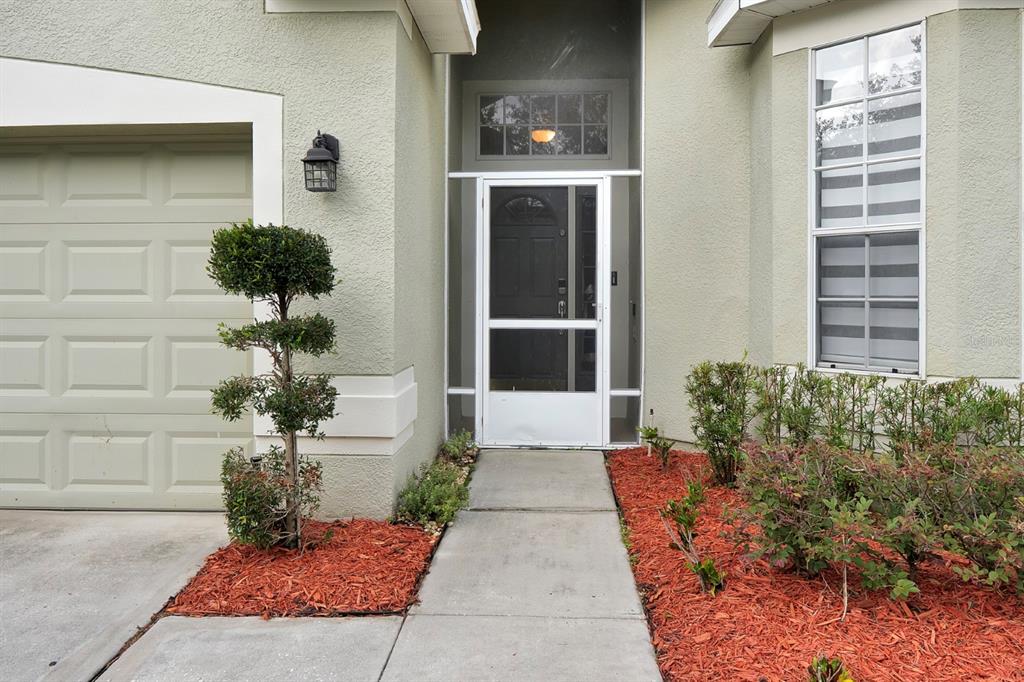 A concrete walkway leads to a front door with a white screen door and garage — 2713 BARNSLEY LANE, KISSIMMEE, FL
