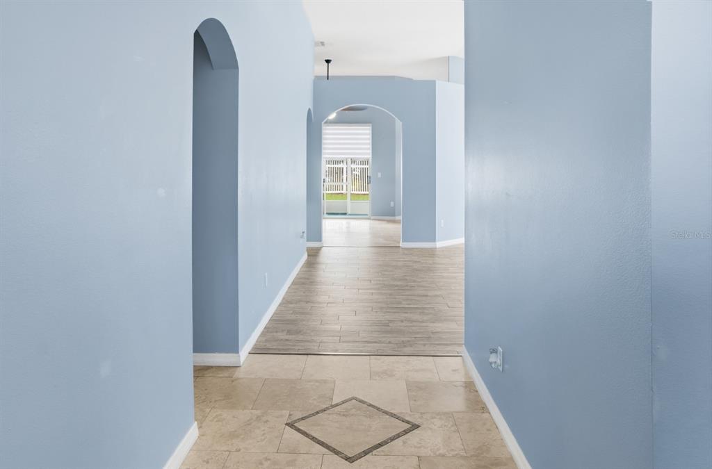 A hallway with light blue walls transitions from tiled flooring to wood-look planks — 2713 BARNSLEY LANE, KISSIMMEE, FL