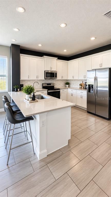 A kitchen features white cabinets, a quartz island with bar seating, and light tile flooring — 2695 NOTTEL DRIVE, ST CLOUD, FL