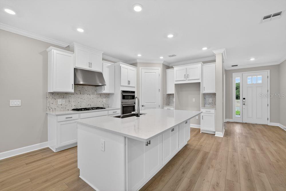A modern kitchen features white cabinetry, a large center island, and light wood-look flooring — 14219 SAWMILL STREET, PARRISH, FL