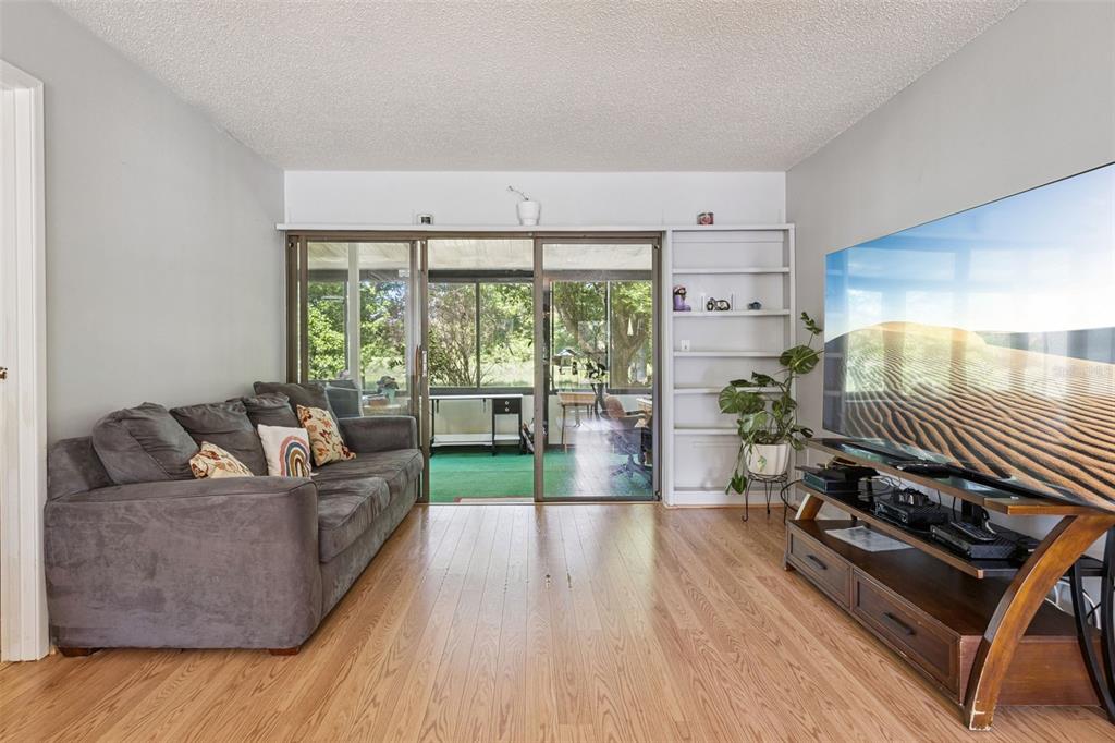 A living room features wood-look flooring, a gray sofa, a television, and sliding glass doors — 50 SHEOAH BOULEVARD UNIT 33, WINTER SPRINGS, FL