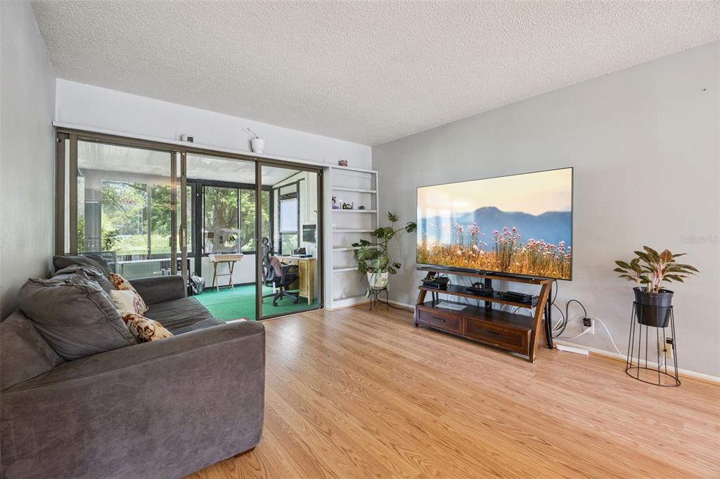 A living room features wood flooring, a gray sofa, a large television, and sliding glass doors — 50 SHEOAH BOULEVARD UNIT 33, WINTER SPRINGS, FL