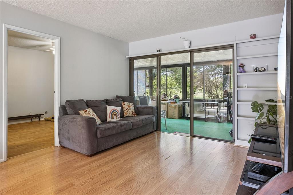 A living room with wood flooring, a gray sofa, built-in shelving, and sliding glass doors — 50 SHEOAH BOULEVARD UNIT 33, WINTER SPRINGS, FL