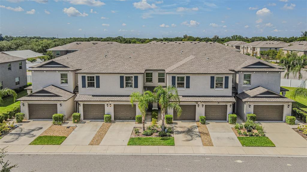 An exterior view of a multi-unit townhouse building with gray stucco walls and brown garages — 817 ROYAL EMPRESS DRIVE, RUSKIN, FL