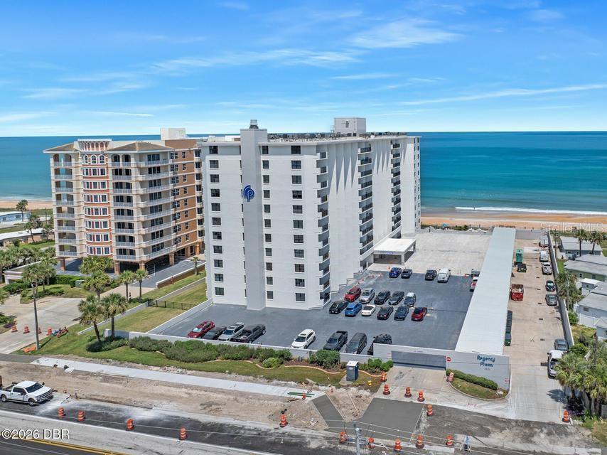 An aerial view shows a tall white apartment building with a parking lot beside the ocean — 1415 OCEAN SHORE BOULEVARD UNIT F110, ORMOND BEACH, FL