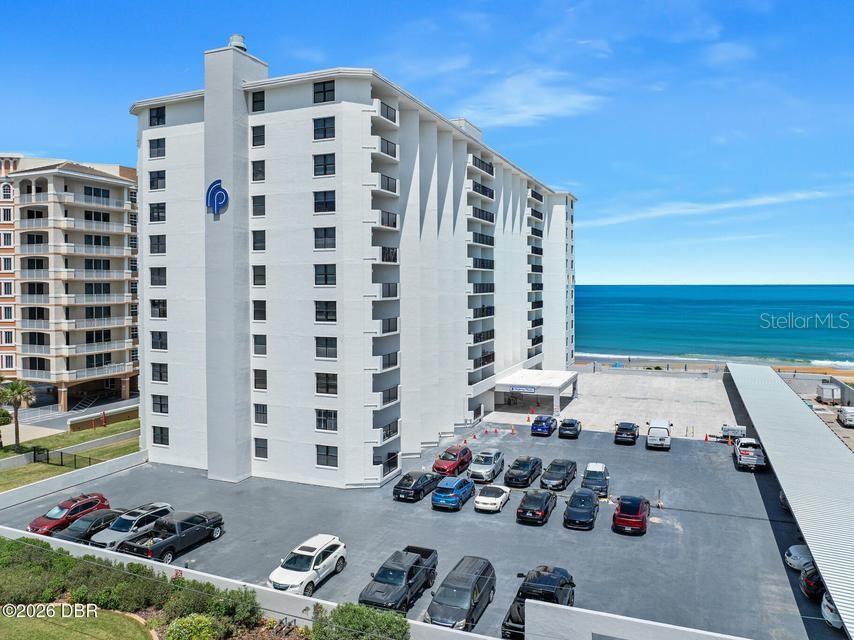 An aerial view shows a multi-story white beachfront condominium building with an adjacent parking lot — 1415 OCEAN SHORE BOULEVARD UNIT F110, ORMOND BEACH, FL
