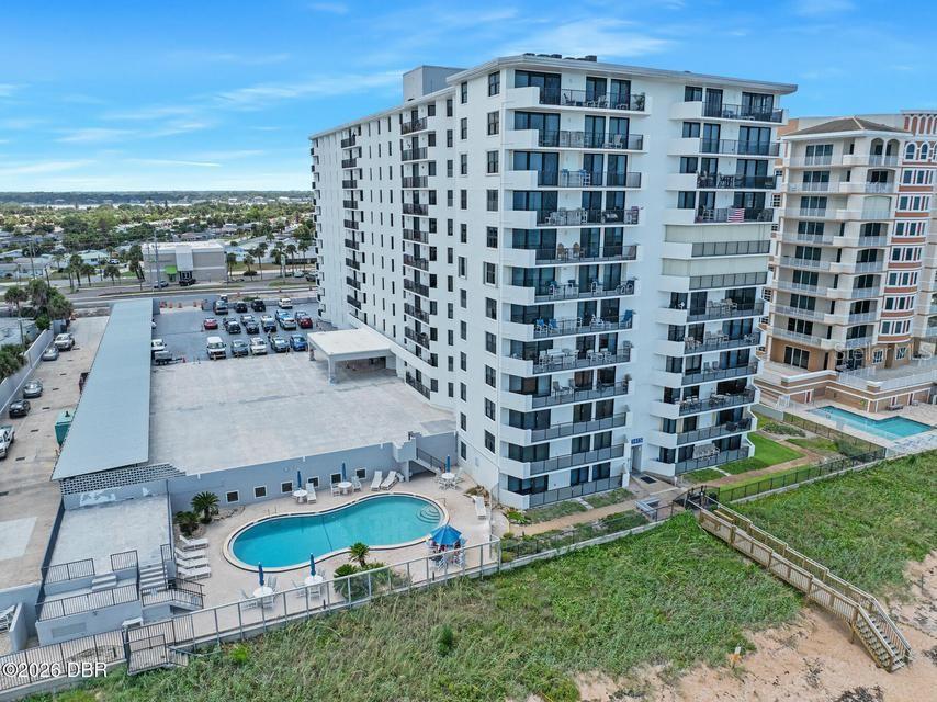 An aerial view shows a tall white apartment building with a pool and parking lot — 1415 OCEAN SHORE BOULEVARD UNIT F110, ORMOND BEACH, FL