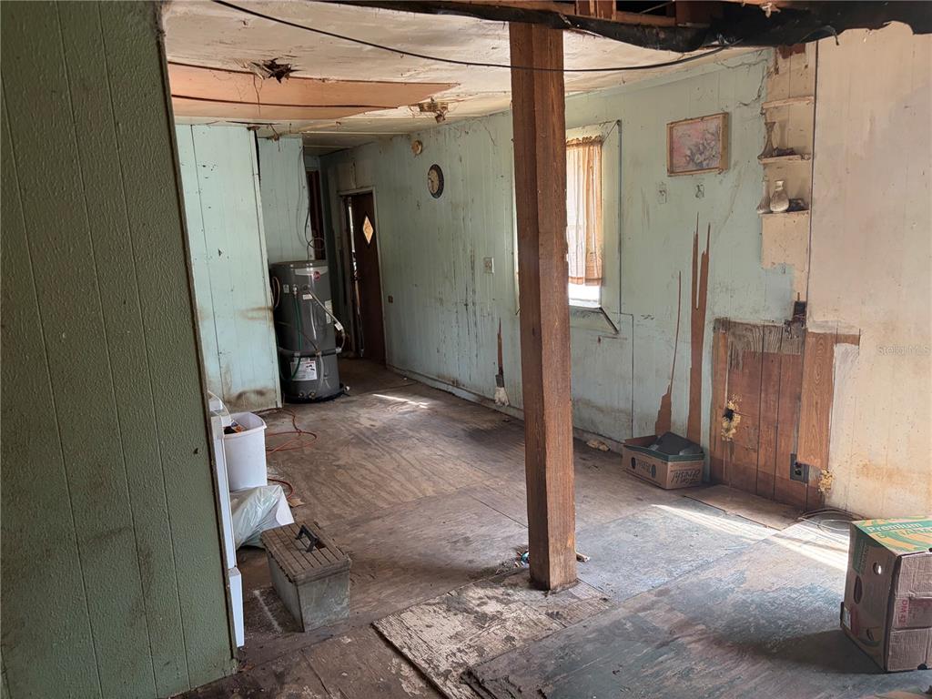 An interior view of a dilapidated room featuring exposed plywood flooring, wood paneling, and a water heater — 8270 NE 117TH PLACE, BRONSON, FL