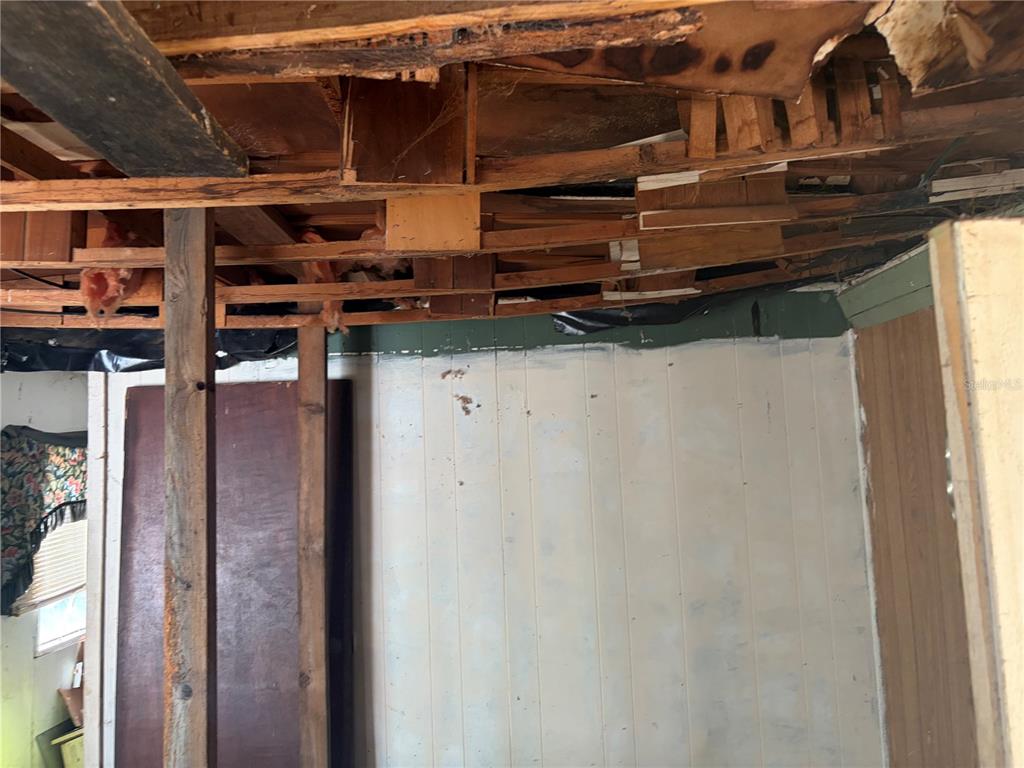 An unfinished room with exposed ceiling joists, wood paneling, and a vertical support beam — 8270 NE 117TH PLACE, BRONSON, FL