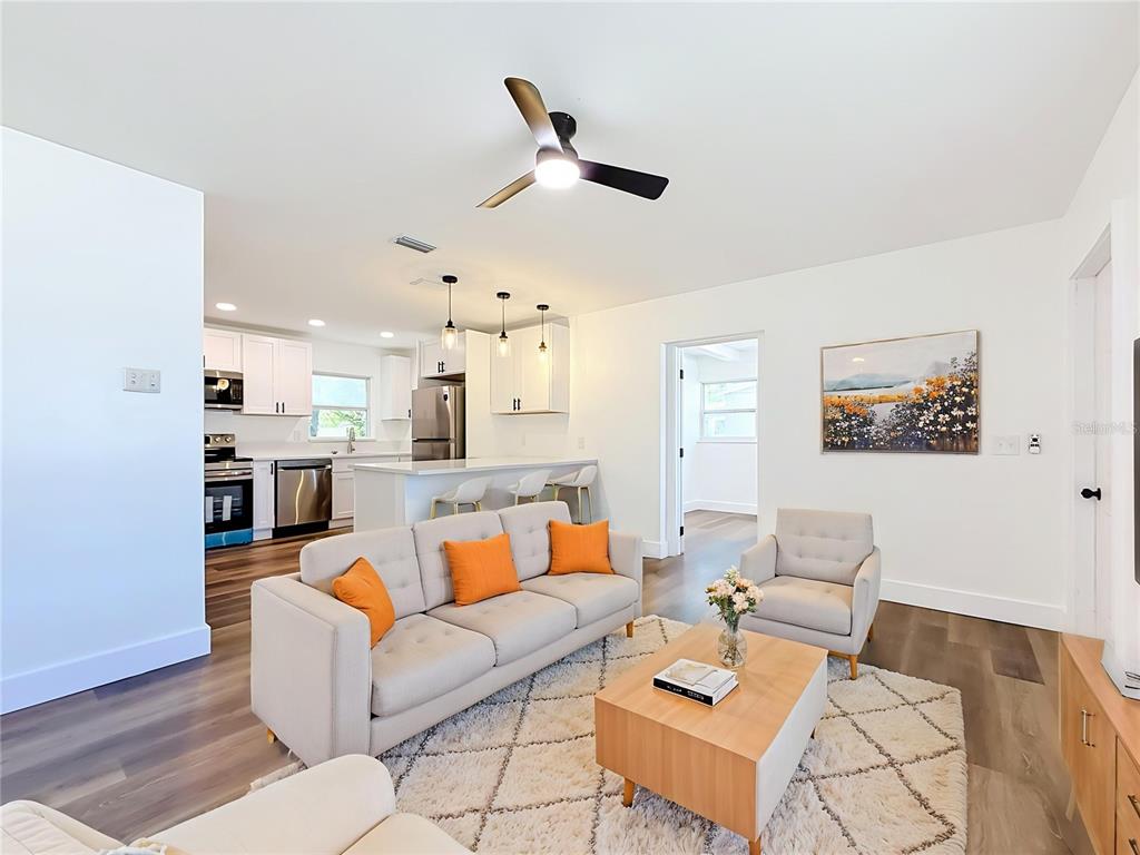 A living room with a beige sofa, orange pillows, and an open kitchen with white cabinets — 6748 78TH AVENUE N, PINELLAS PARK, FL