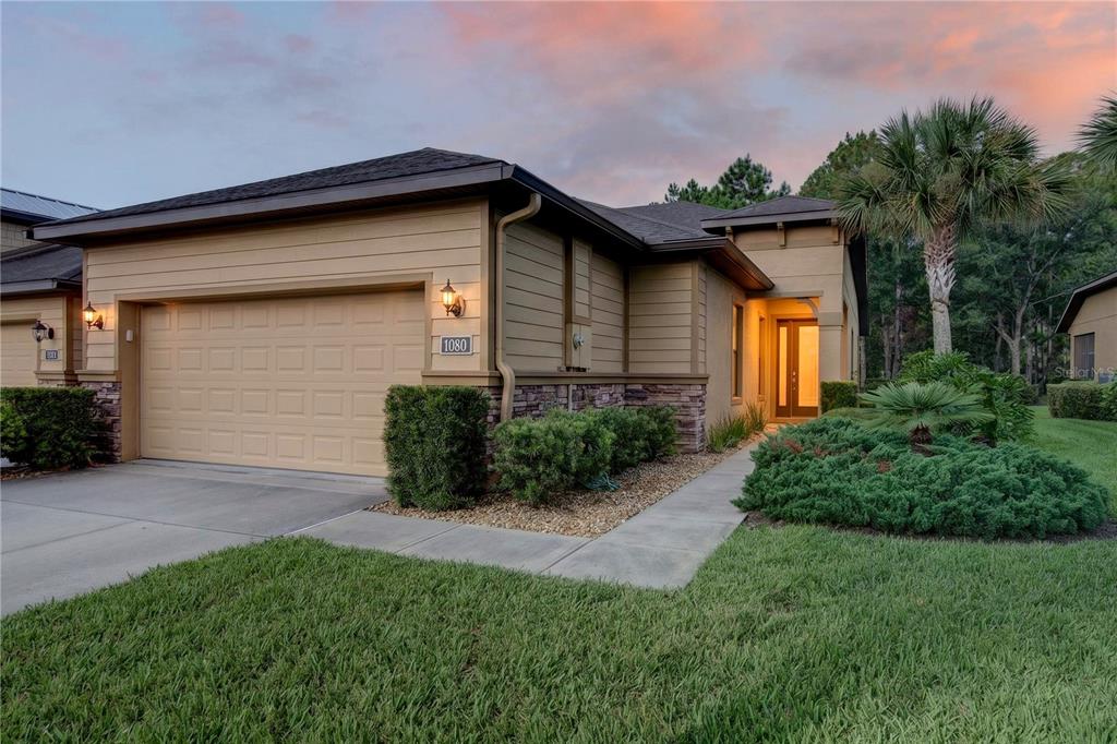A tan single-story house with a two-car garage, stone accents, and a landscaped front yard — 1080 KILKENNY LANE, ORMOND BEACH, FL