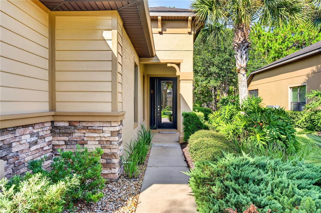 A concrete walkway leads to the front entrance of a house with stone and siding — 1080 KILKENNY LANE, ORMOND BEACH, FL