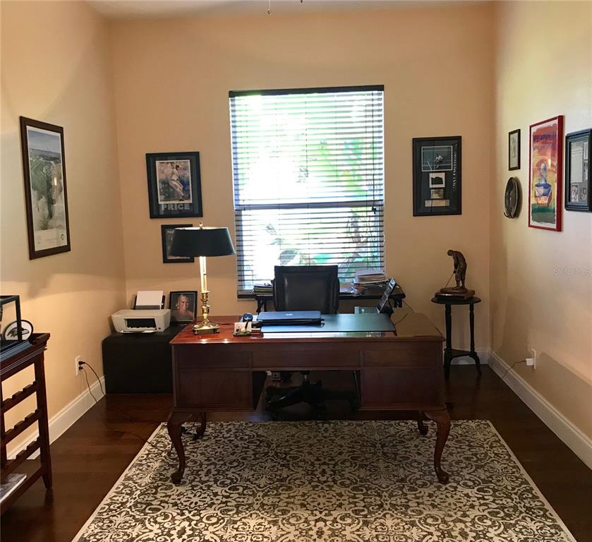 A home office features a wooden desk, a patterned rug, and several framed wall decorations — 6273 DONNINGTON COURT, SARASOTA, FL