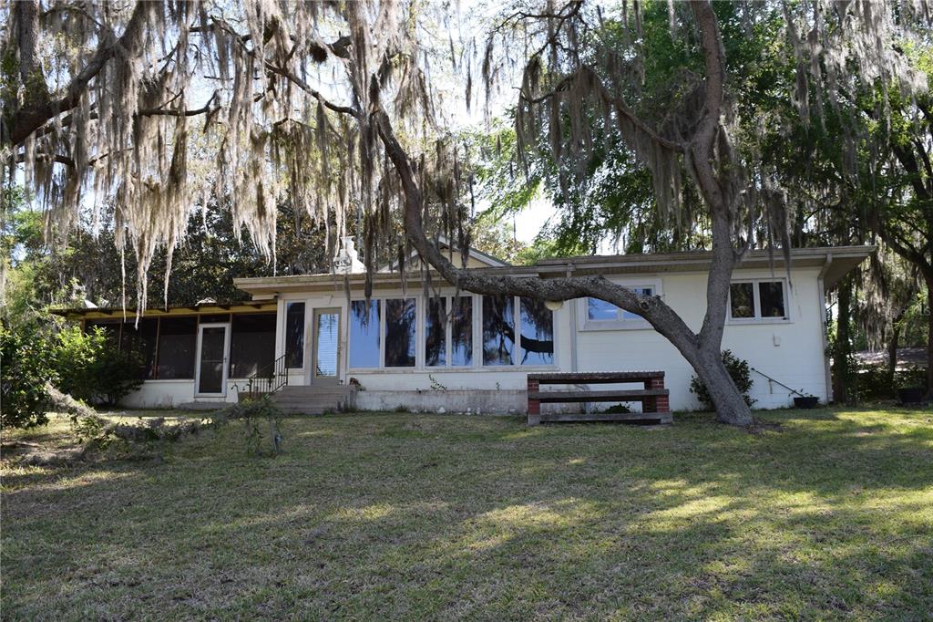 A single-story house with a screened porch and large windows sits under moss-draped trees — 121 AWEEMA WAY, MELROSE, FL