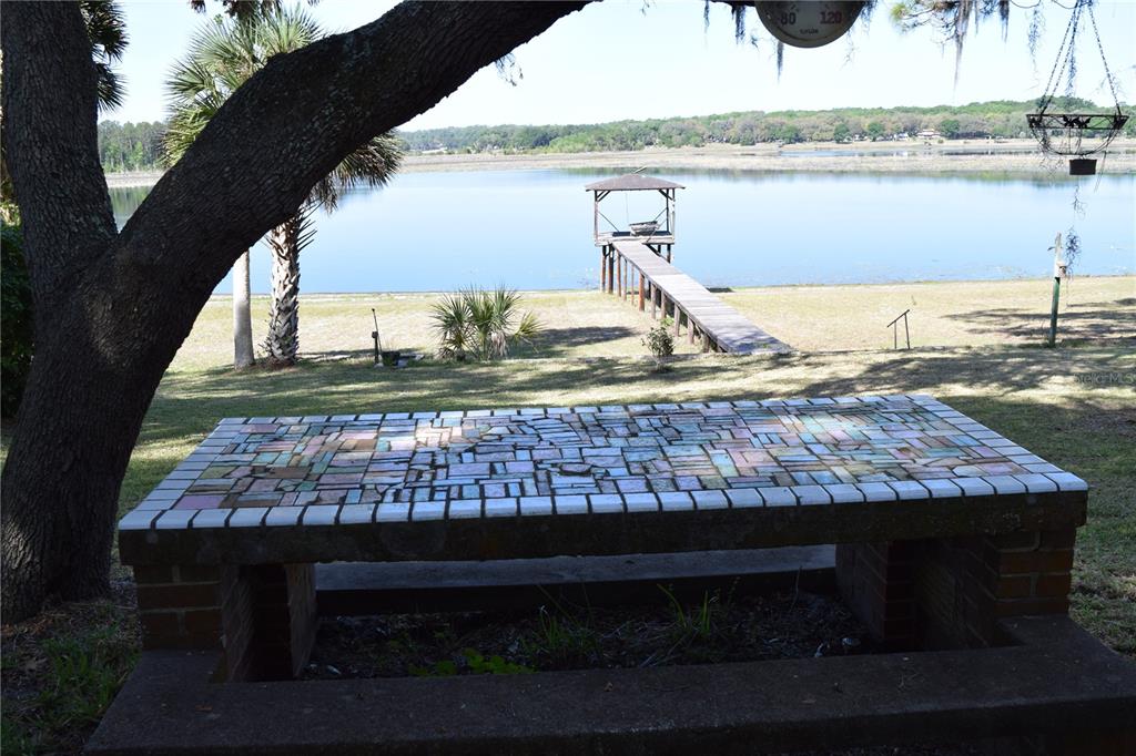 A mosaic-tiled table sits in a yard overlooking a wooden dock on a lake — 121 AWEEMA WAY, MELROSE, FL