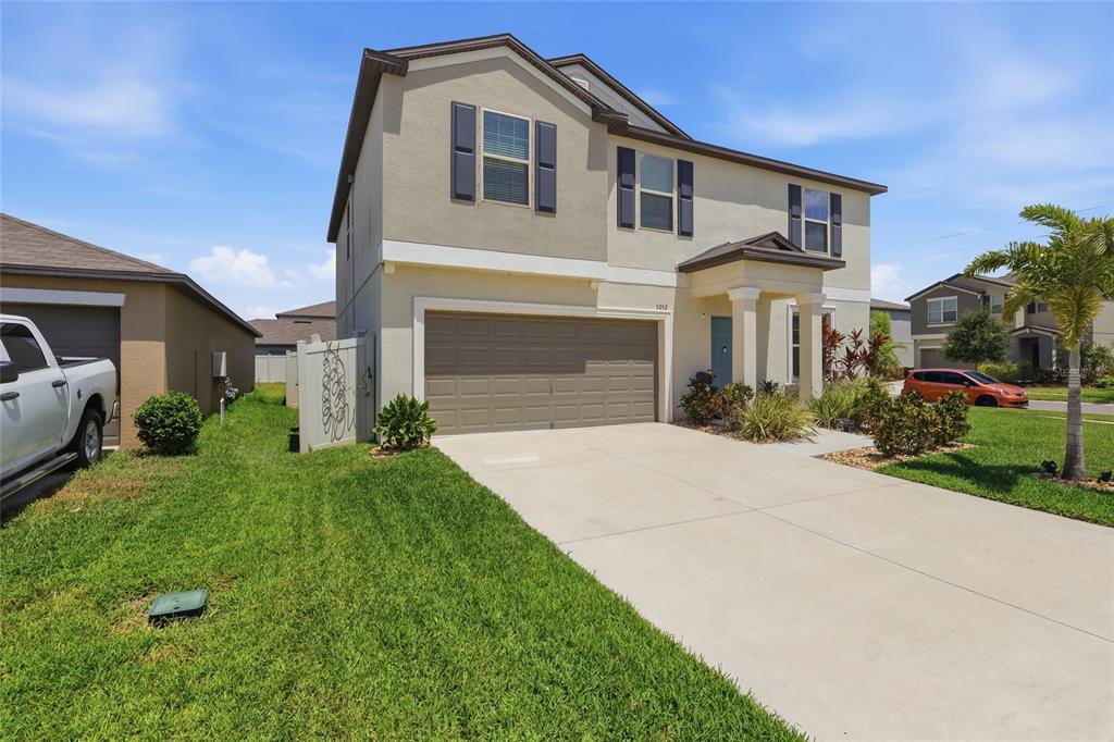 A two-story suburban house with a beige stucco exterior, a two-car garage, and a driveway — 5052 WHITE CHICORY DRIVE, APOLLO BEACH, FL