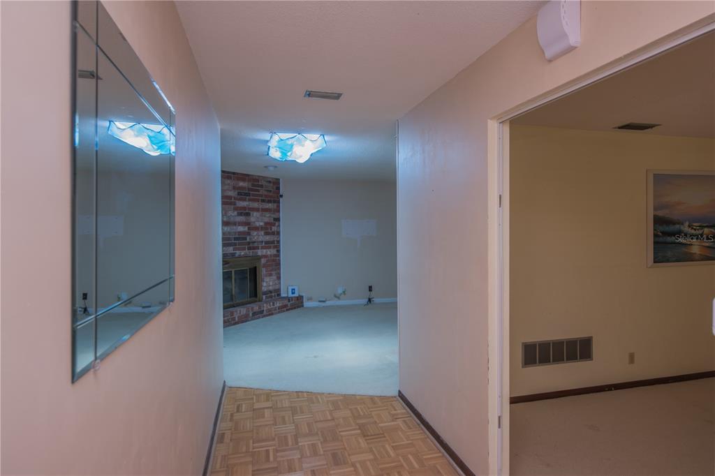 A hallway with parquet flooring leads to a living room featuring a brick fireplace — 34 OAKMONT CIRCLE, ORMOND BEACH, FL