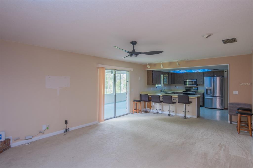 A living room with beige carpet and a ceiling fan opens to a kitchen with bar seating — 34 OAKMONT CIRCLE, ORMOND BEACH, FL