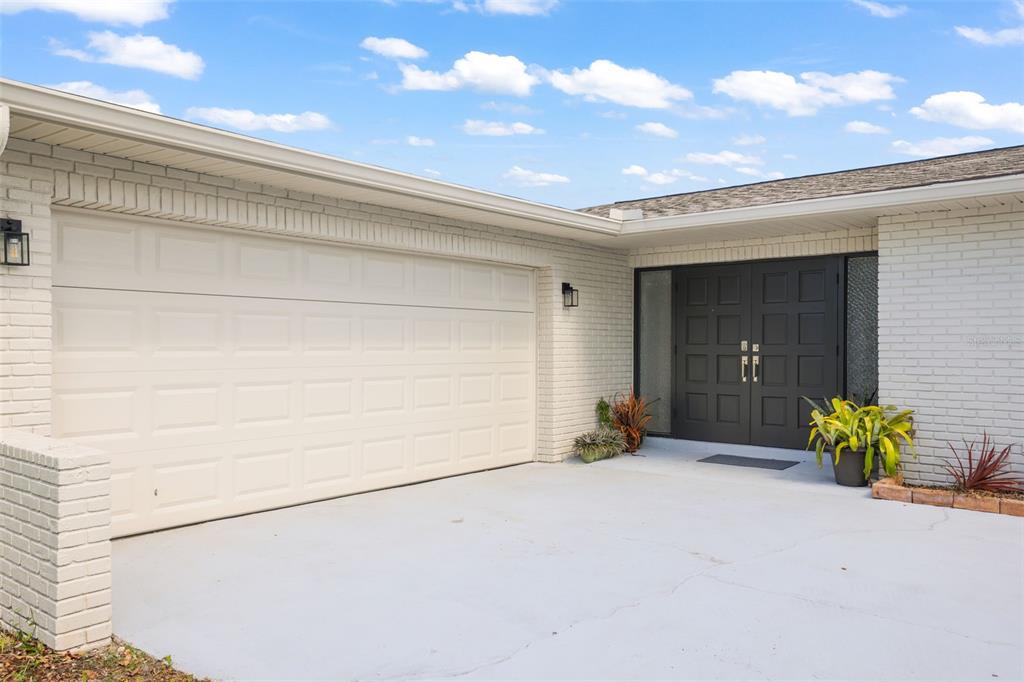 A white brick house exterior features a double garage door and a dark double front door — 13635 97TH TERRACE, SEMINOLE, FL