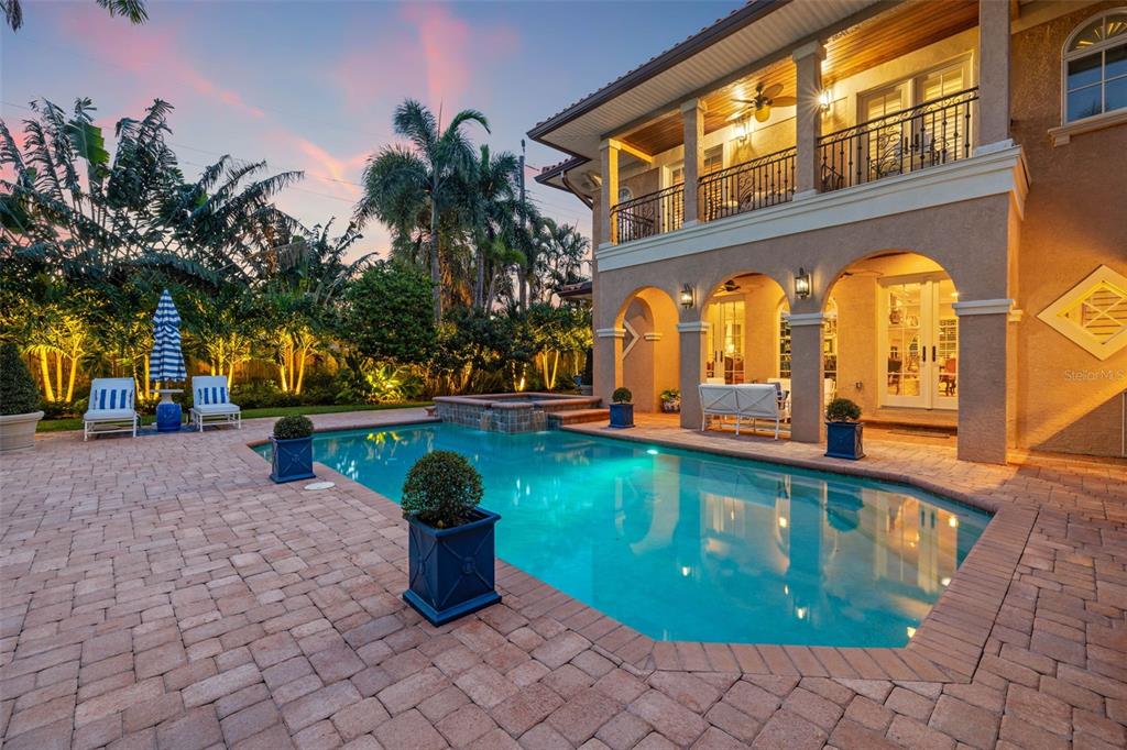 A backyard patio features a swimming pool, a raised hot tub, and palm trees at dusk — 1124 SEVILLE LANE NE, ST PETERSBURG, FL