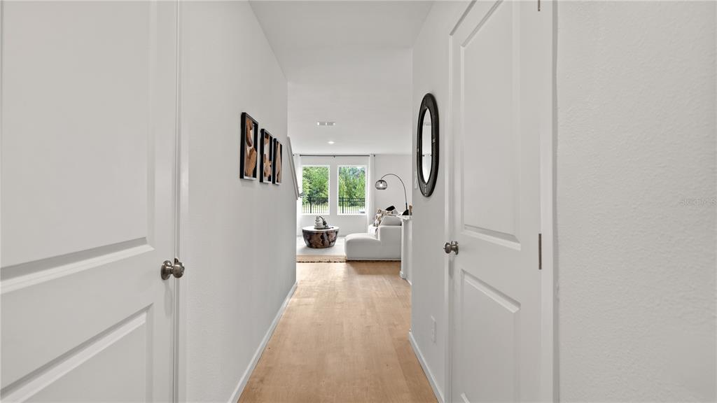 A hallway with white walls and light wood flooring leads toward a bright living area — 2886 CREEKSIDE ROAD, HAINES CITY, FL