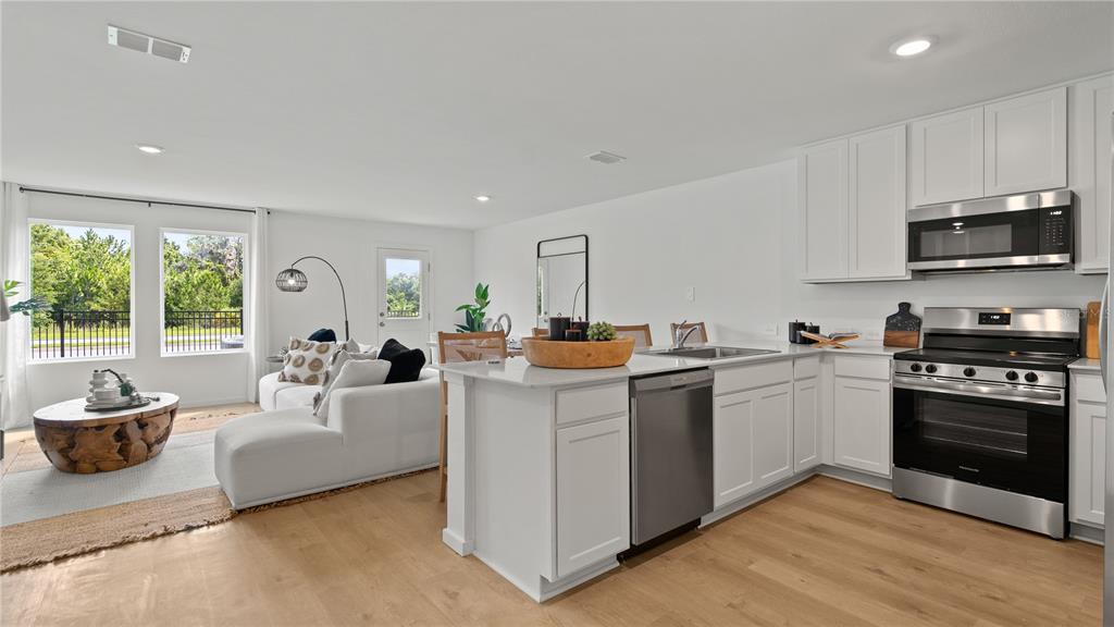 A bright, open-concept kitchen and living area features white cabinetry, stainless steel appliances, and wood-look flooring — 2886 CREEKSIDE ROAD, HAINES CITY, FL