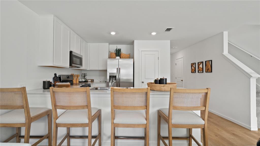 A modern kitchen features white cabinetry, stainless steel appliances, and three wooden bar stools — 2886 CREEKSIDE ROAD, HAINES CITY, FL