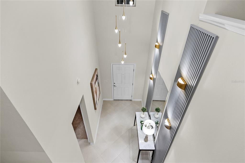 A high-ceilinged entryway features a white front door, a modern chandelier, and decorative wall panels — 15961 CAPE CORAL LOOP, CLERMONT, FL