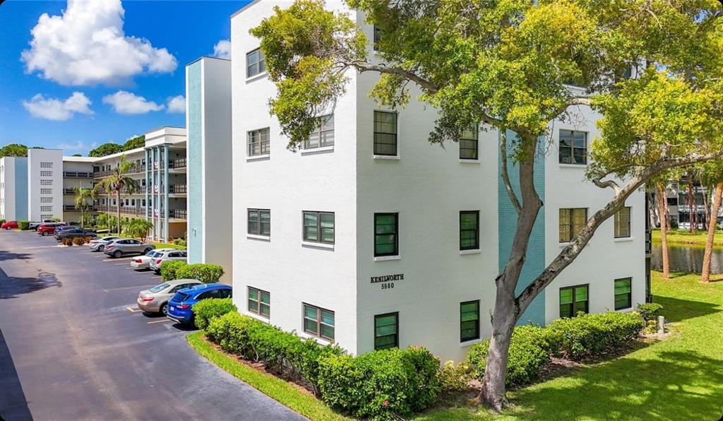An exterior view of a white multi-story apartment building with a parking lot and landscaping — 5980 80TH STREET N UNIT 205, ST PETERSBURG, FL