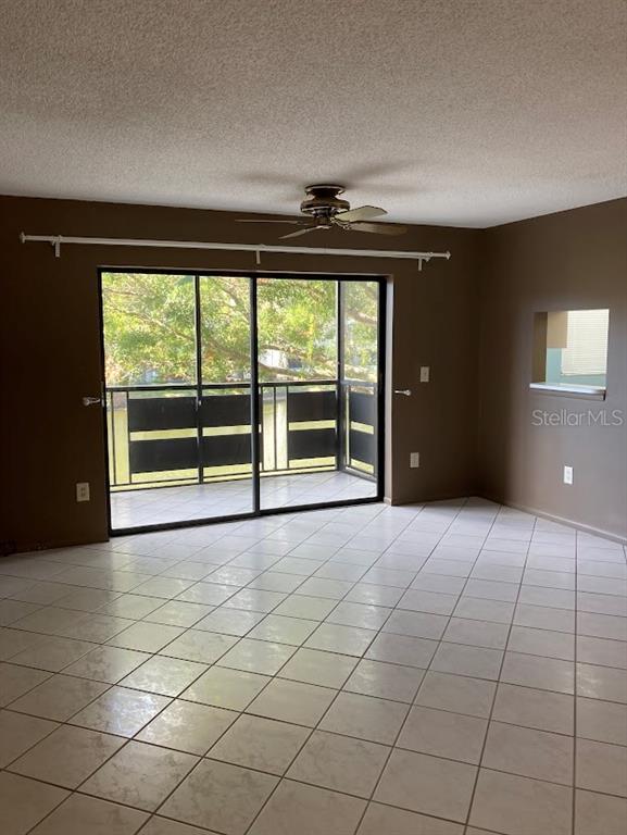 A living room with light-colored tile floors, brown walls, a ceiling fan, and sliding glass doors — 5980 80TH STREET N UNIT 205, ST PETERSBURG, FL