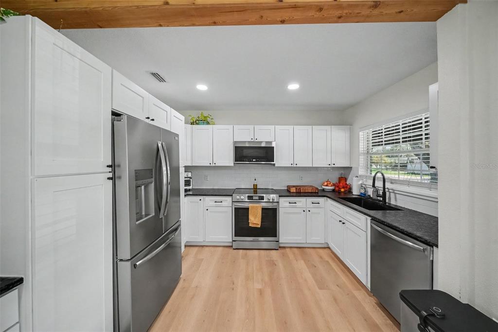 An open-concept kitchen and living area features white cabinetry, wood ceiling beams, and light flooring — 4636 W BAY COURT AVENUE, TAMPA, FL