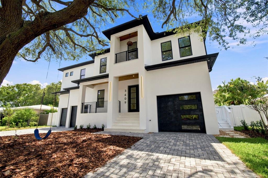 A modern two-story white house with a black garage door, balcony, and a front yard swing — 3609 S GARDENIA AVENUE, TAMPA, FL