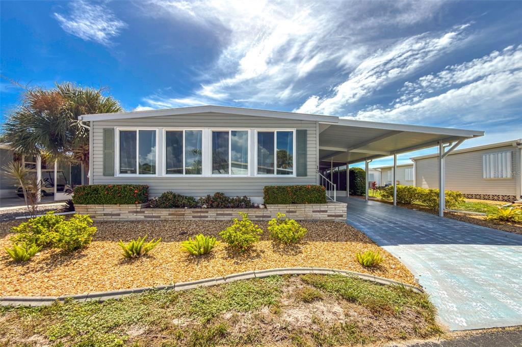 A single-story manufactured home with light gray siding, a carport, and a landscaped front yard — 13 S MARINA PLAZA, ENGLEWOOD, FL