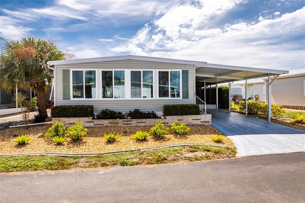 A light gray manufactured home with a carport and landscaped front yard under a blue sky — 13 S MARINA PLAZA, ENGLEWOOD, FL
