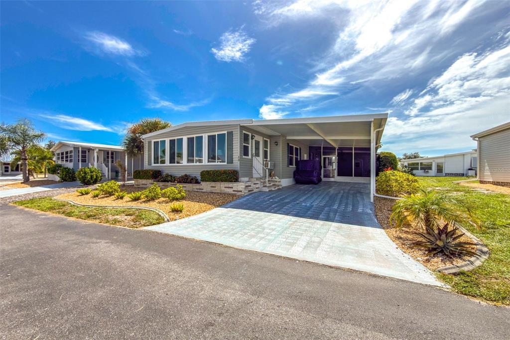 A single-story manufactured home with a carport, light gray siding, and a landscaped front yard — 13 S MARINA PLAZA, ENGLEWOOD, FL