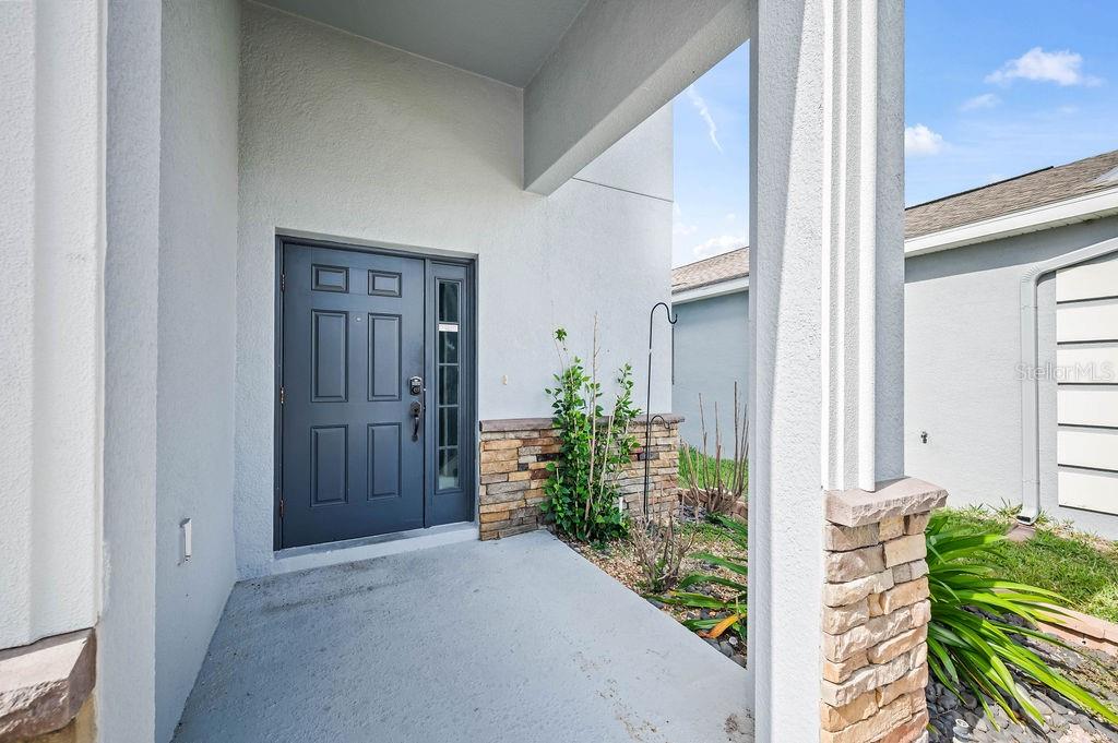 A covered front porch features a dark gray door with a side window and stone accents — 4538 CORTLAND DRIVE, DAVENPORT, FL