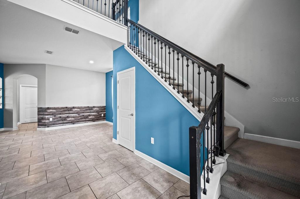 A foyer with tiled floors, a blue accent wall, and a carpeted staircase with iron railings — 4538 CORTLAND DRIVE, DAVENPORT, FL