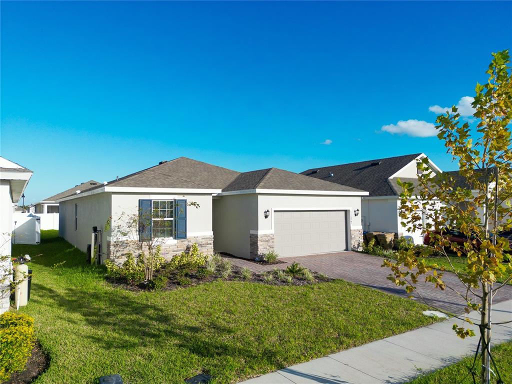 A single-story house with a beige stucco exterior, stone accents, and a two-car garage — 1177 FOX HEDGE LANE, ST CLOUD, FL
