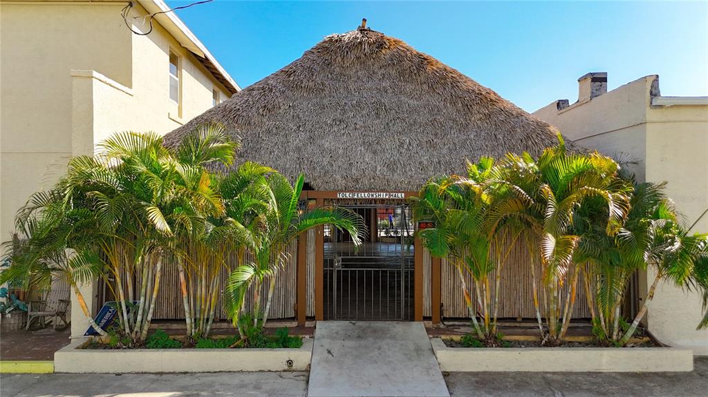 An exterior view of a building entrance with a thatched roof and palm trees — 1001 MANATEE AVENUE E, BRADENTON, FL