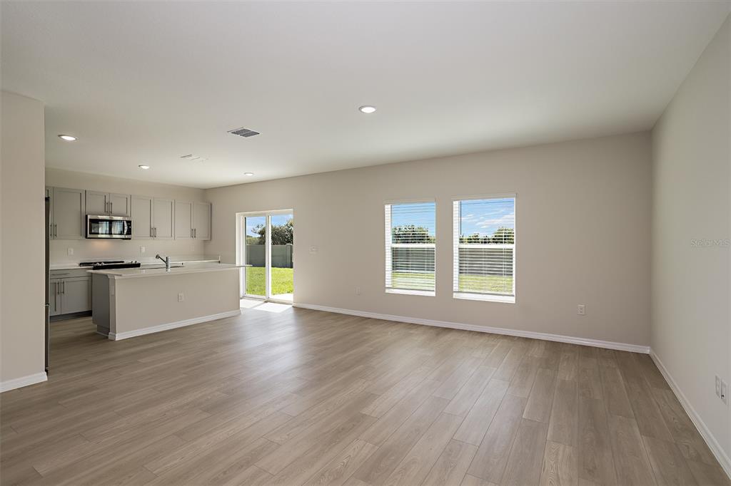 An open-concept kitchen and living area features light wood-look flooring and gray cabinetry — 2151 LAWSON WAY, ZEPHYRHILLS, FL