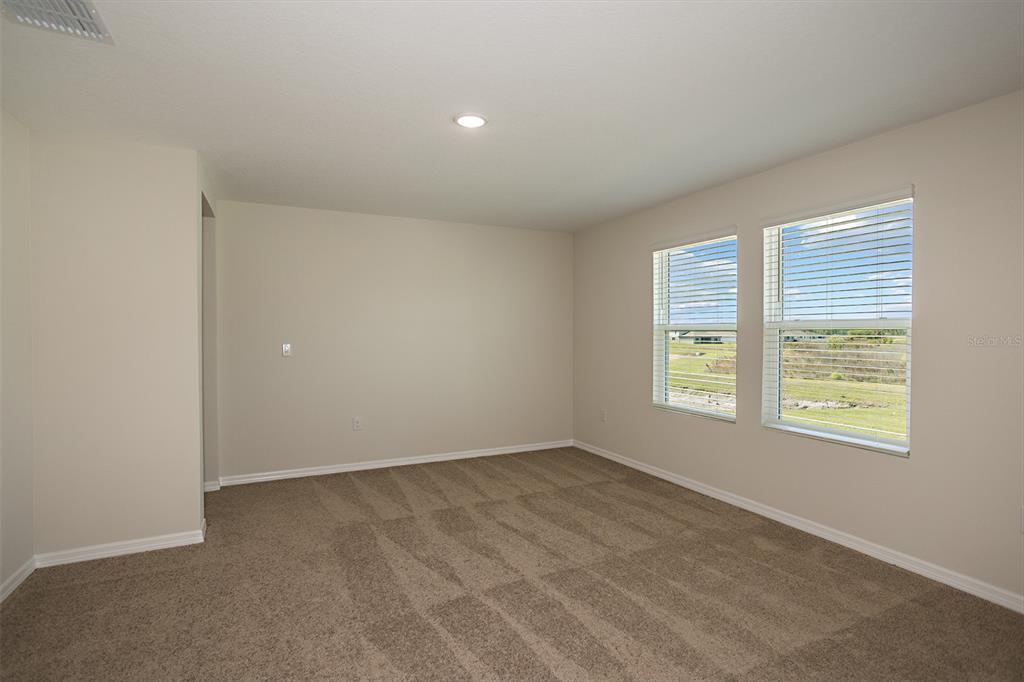 An empty bedroom with beige walls, tan carpet, and two windows overlooking a grassy field — 2151 LAWSON WAY, ZEPHYRHILLS, FL