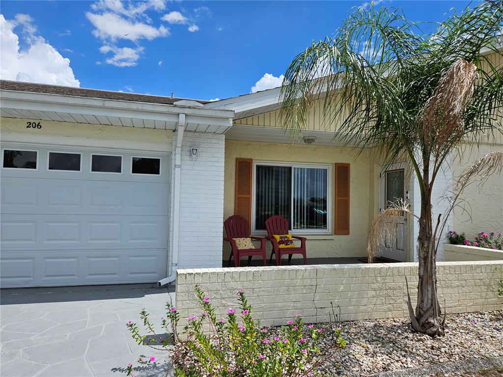 A single-story house exterior features a white garage, a small patio with two chairs, and a palm tree — 206 SOLA LANE, SUN CITY CENTER, FL