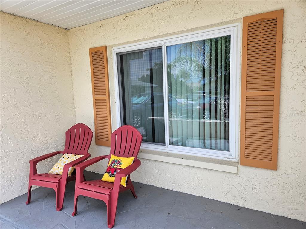 Two red Adirondack chairs sit on a covered patio in front of a window with shutters — 206 SOLA LANE, SUN CITY CENTER, FL
