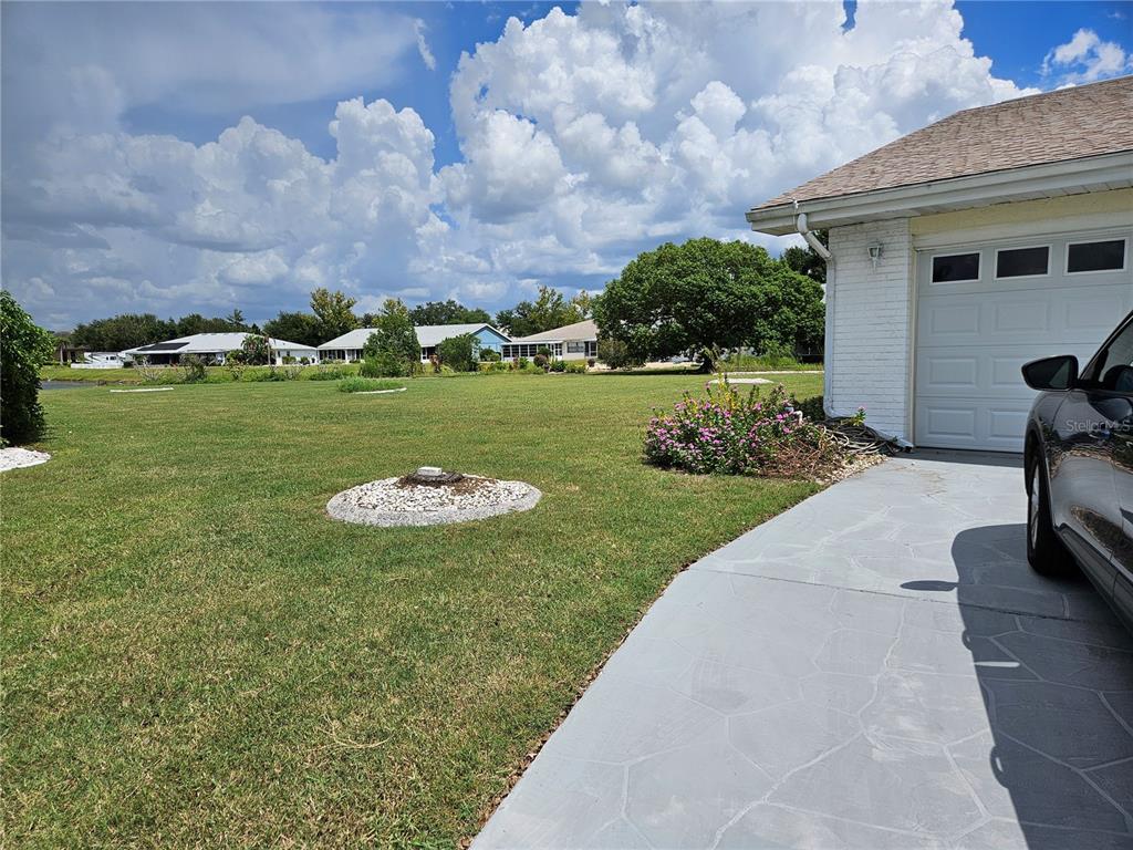 A view of a grassy yard with a circular stone feature and a paved driveway — 206 SOLA LANE, SUN CITY CENTER, FL